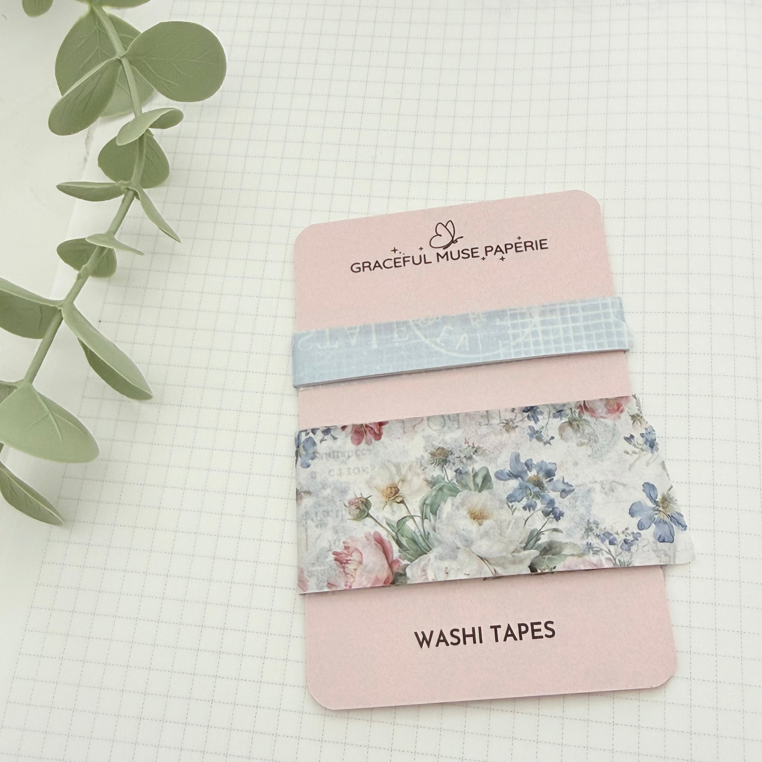 A set of washi tapes by Graceful Muse Papierie, displayed on their pink packaging card. The tapes include a light blue patterned stripe, a floral tape with blue, pink, and white flowers, and a solid pale pink tape.